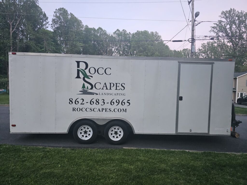 Rocc Scapes Landscaping logo, phone number and website lettering on the driver side of a cargo trailer, Mt Olive NJ